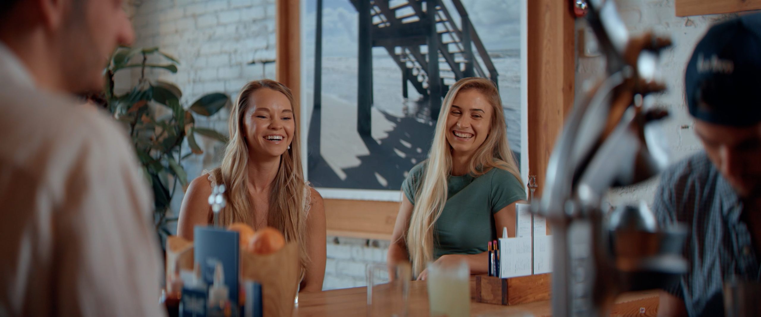 Two women laughing at a table in a Bartaco dining room — still from the brand film